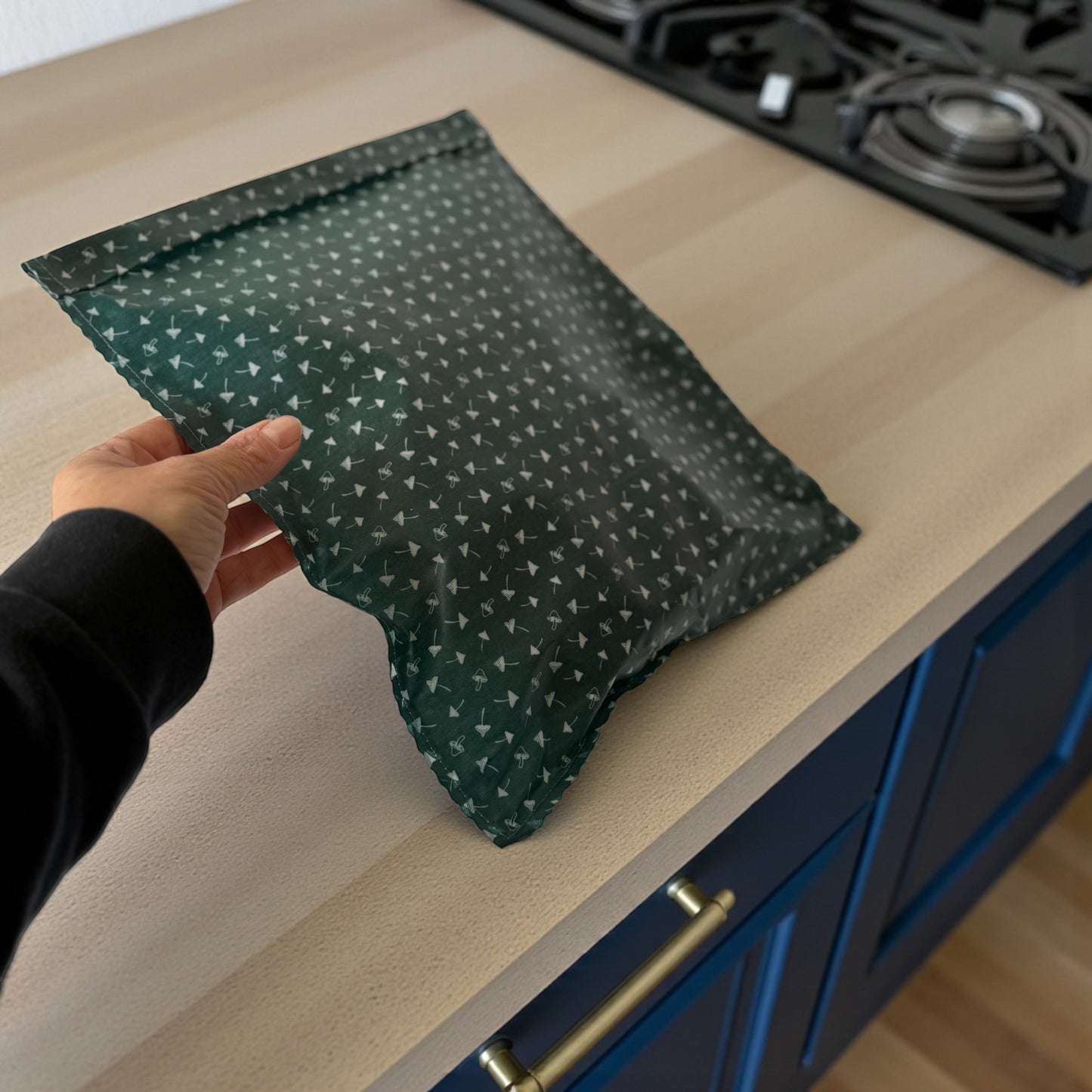 Green patterned bag held by a hand on a kitchen counter with blue cabinets.